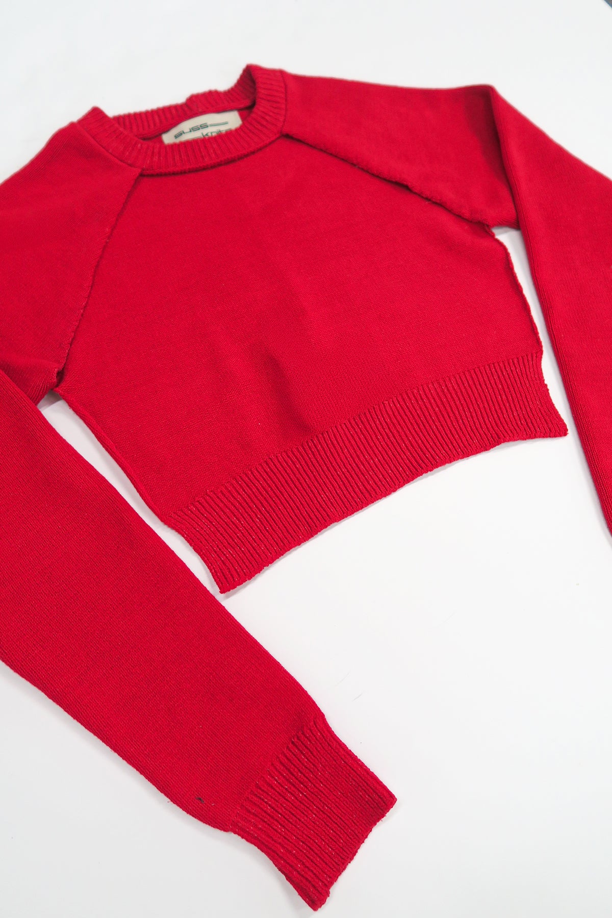 The Suss Knits bright Red Open Raglan Knit Top angled flat lay showing ribbed hem and cuff with cut out front detail.