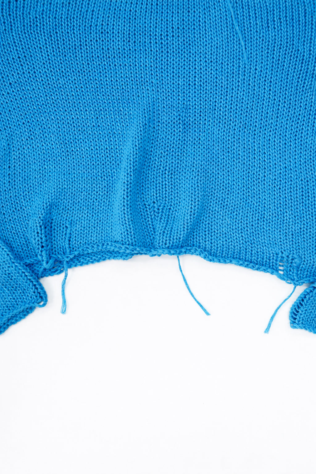 Raw hem detail of soft lightweight knit sweater hand loomed in turquoise recycled cotton yarn
