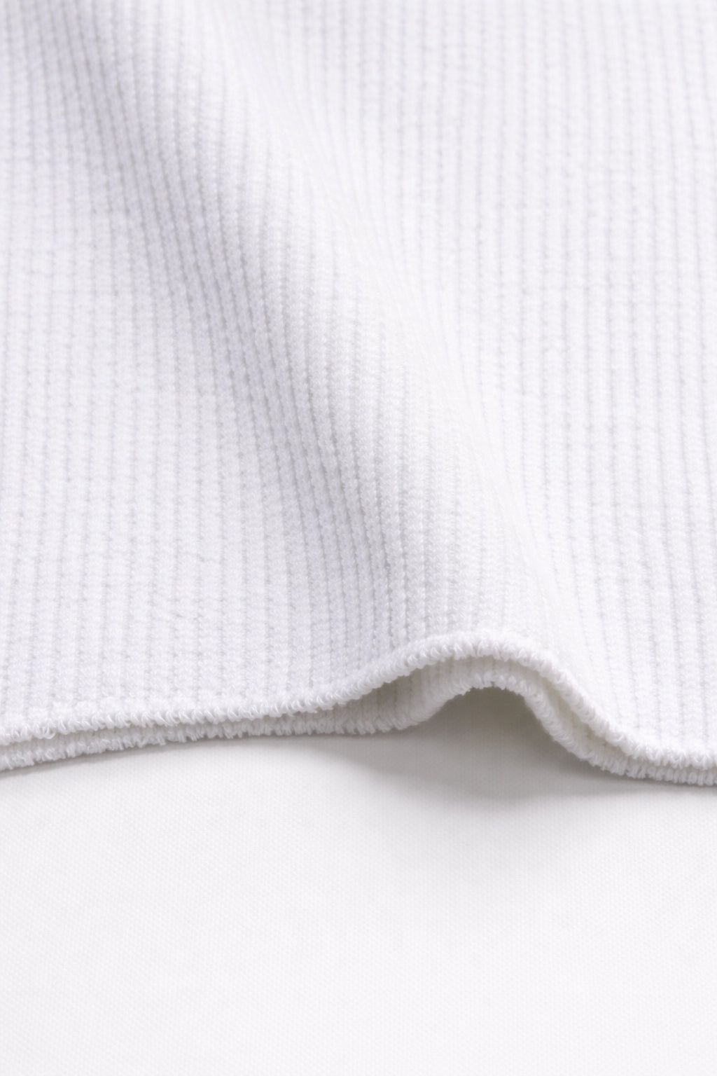 Close-up of ribbed texture and curved hem on white knit tank in recycled cotton blend