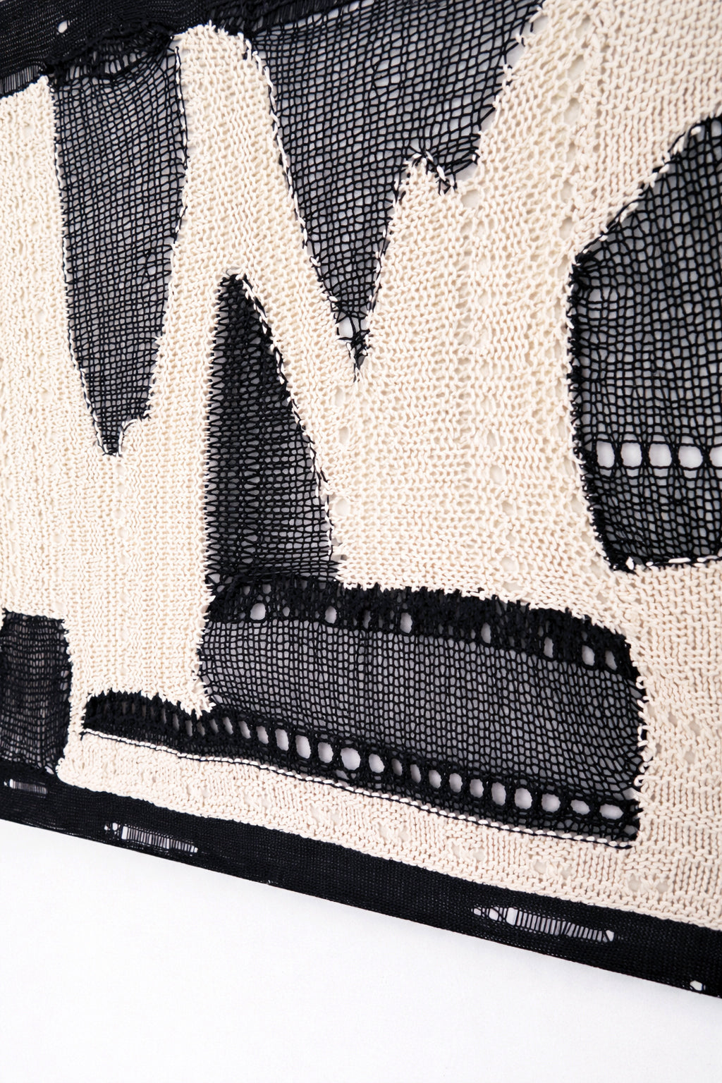 Layered textile detail showing hand knit, crocheted, and mesh elements in tonal black and cream abstract composition