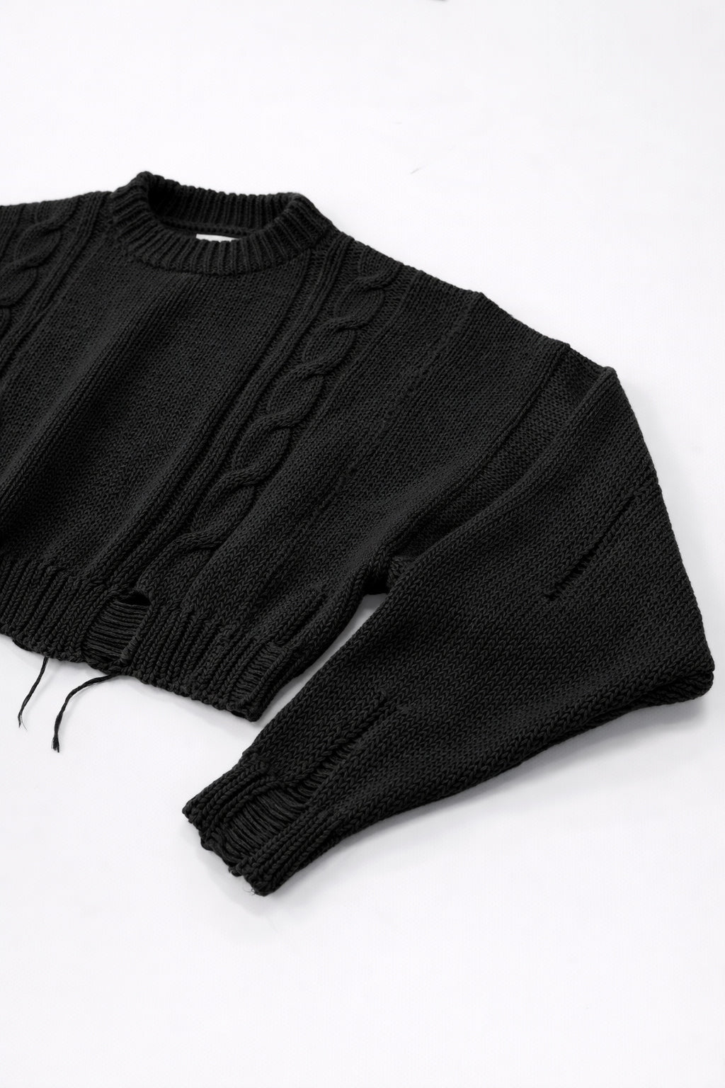 Close up of sleeve on black cropped knit sweater showing angle texture and distressed stitch detail