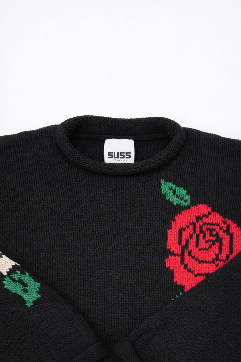 Collar and label detail of black cotton knit sweater with rose design by Suss Knits