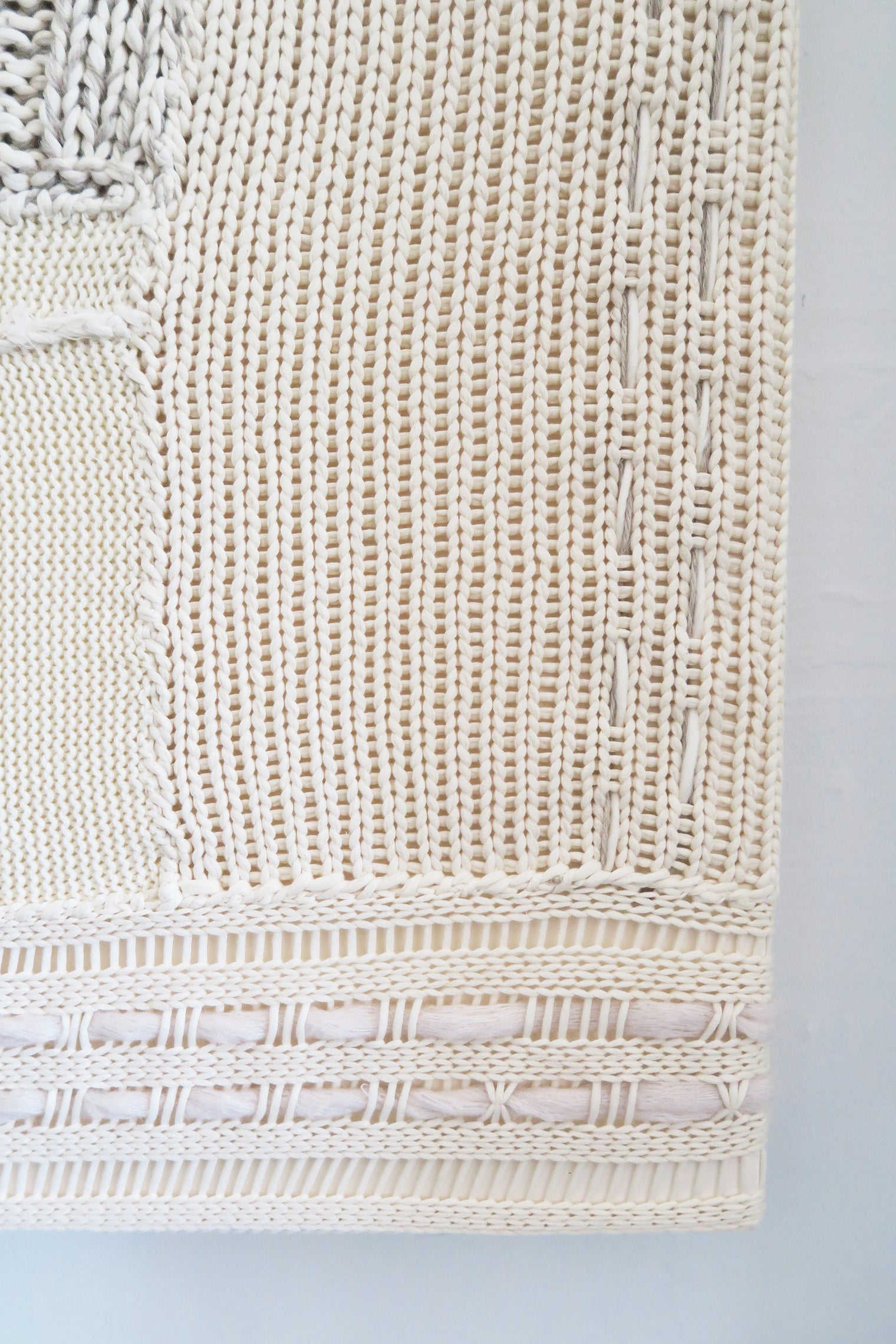 Close-up of right corner hand knit patchwork textile wall art showing mixed stitch patterns and textures in neutral cream tones
