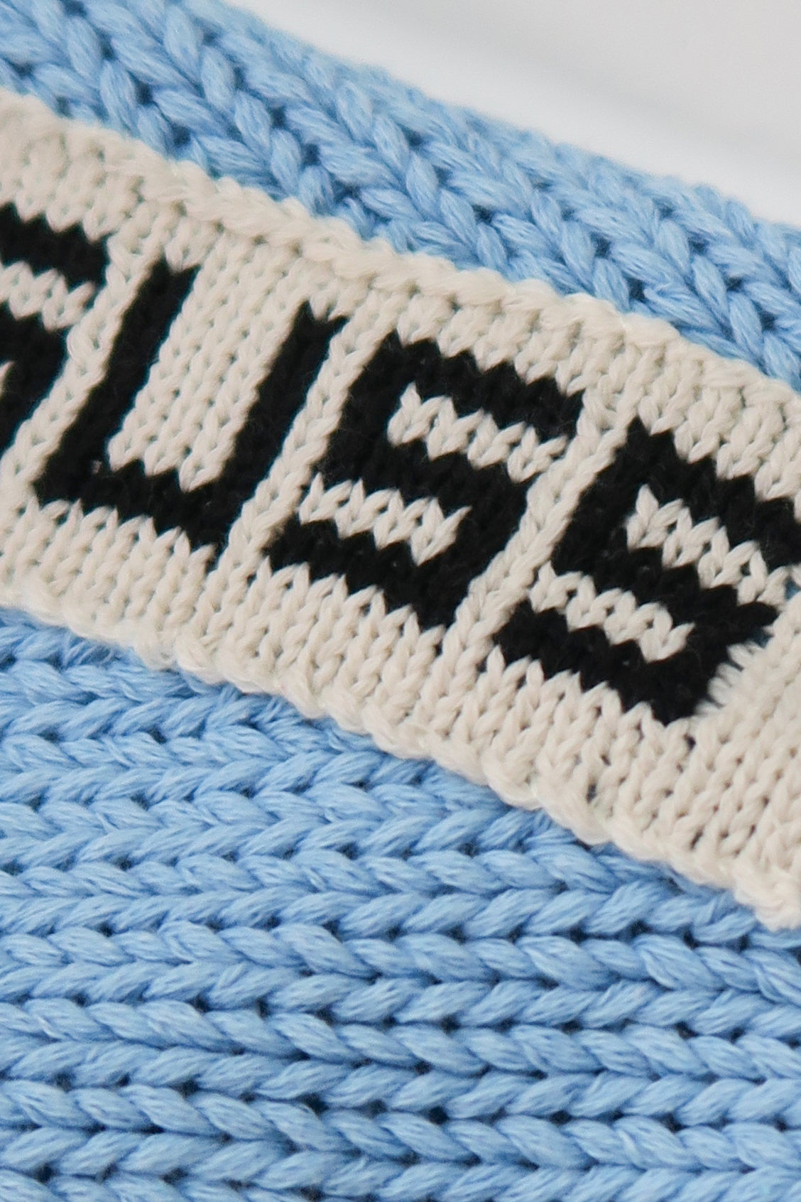 Subtle hand loomed cotton SUSS logo on wrist seam of oversized knit sweater close up