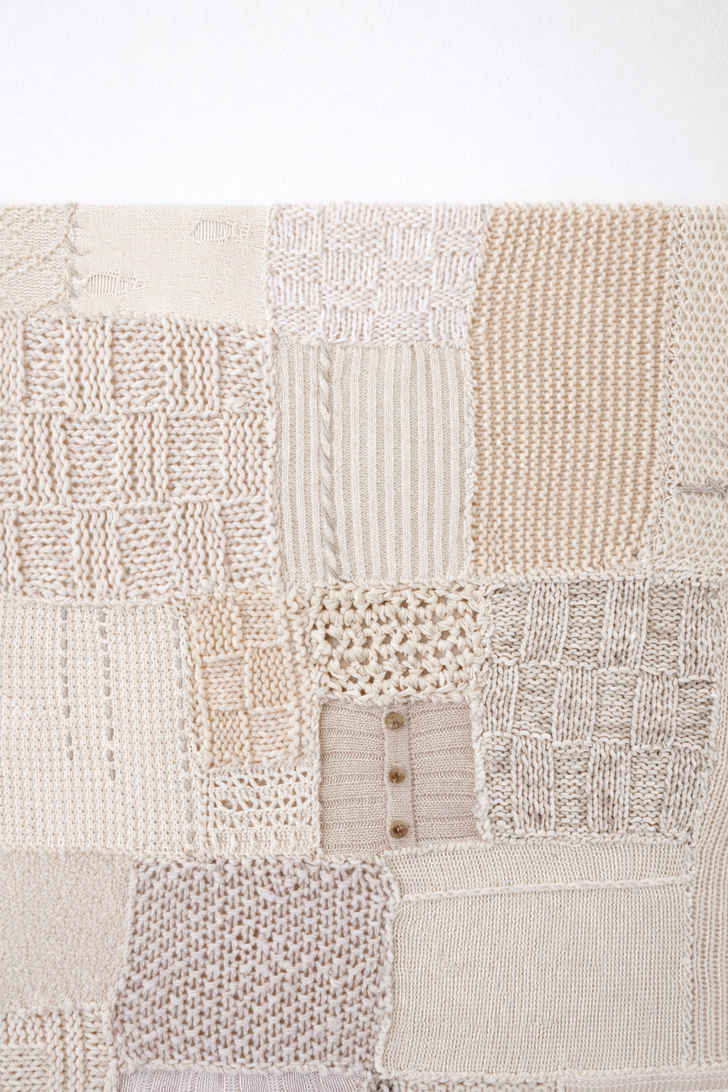 Close-up of hand knit patchwork textile wall art showing mixed stitch patterns and textures in neutral cream tones