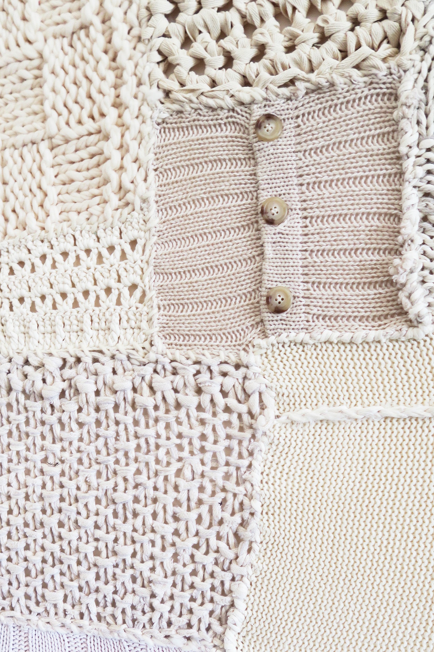 Close-up of hand knit patchwork textile wall art and button swatch showing mixed stitch patterns and textures in neutral cream tones