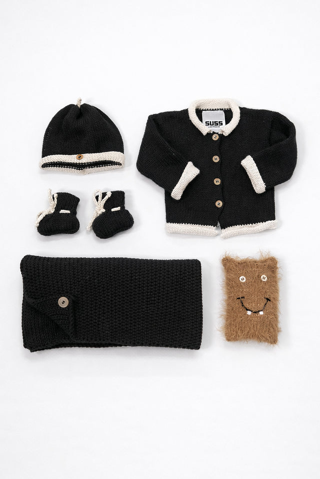 Black and cream cotton baby knit gift set flat lay including cardigan, blanket, beanie, booties and plush toy