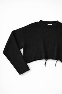 Close-up of black knit sweater sleeve angled showing soft textured stitch