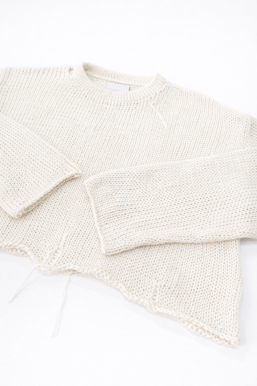 Angle detail of sleeves and distressed hem on cream cropped lightweight sweater