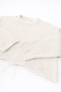 Angle detail of sleeves and distressed hem on cream cropped lightweight sweater