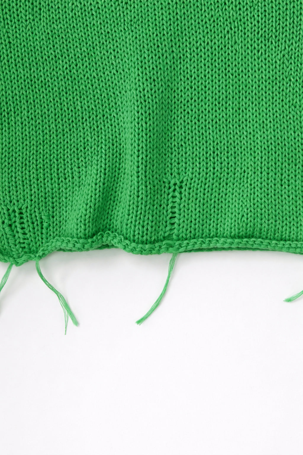 Close up detail of raw hem hand loomed green sweater with drop stitches