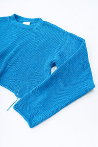 Angle detail shot of turquoise cotton knit light weight sweater with raw edges