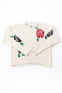 Front flat lay image of the Suss cotton rollneck sweater featuring hand loomed roses in black and red on a cream base