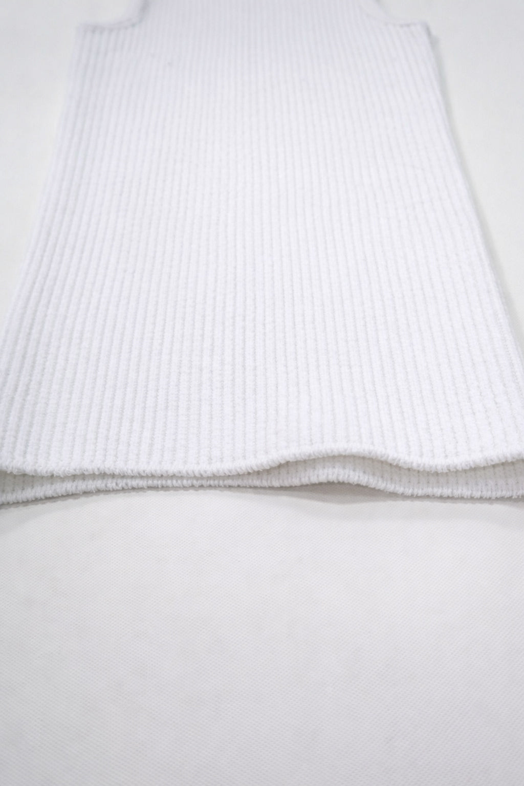 Flat lay detail of white knit tank hem showing textured ribbing and soft structure