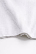 Close-up of ribbed texture and curved hem on white knit tank in recycled cotton blend