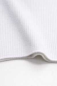 Close-up of ribbed texture and curved hem on white knit tank in recycled cotton blend