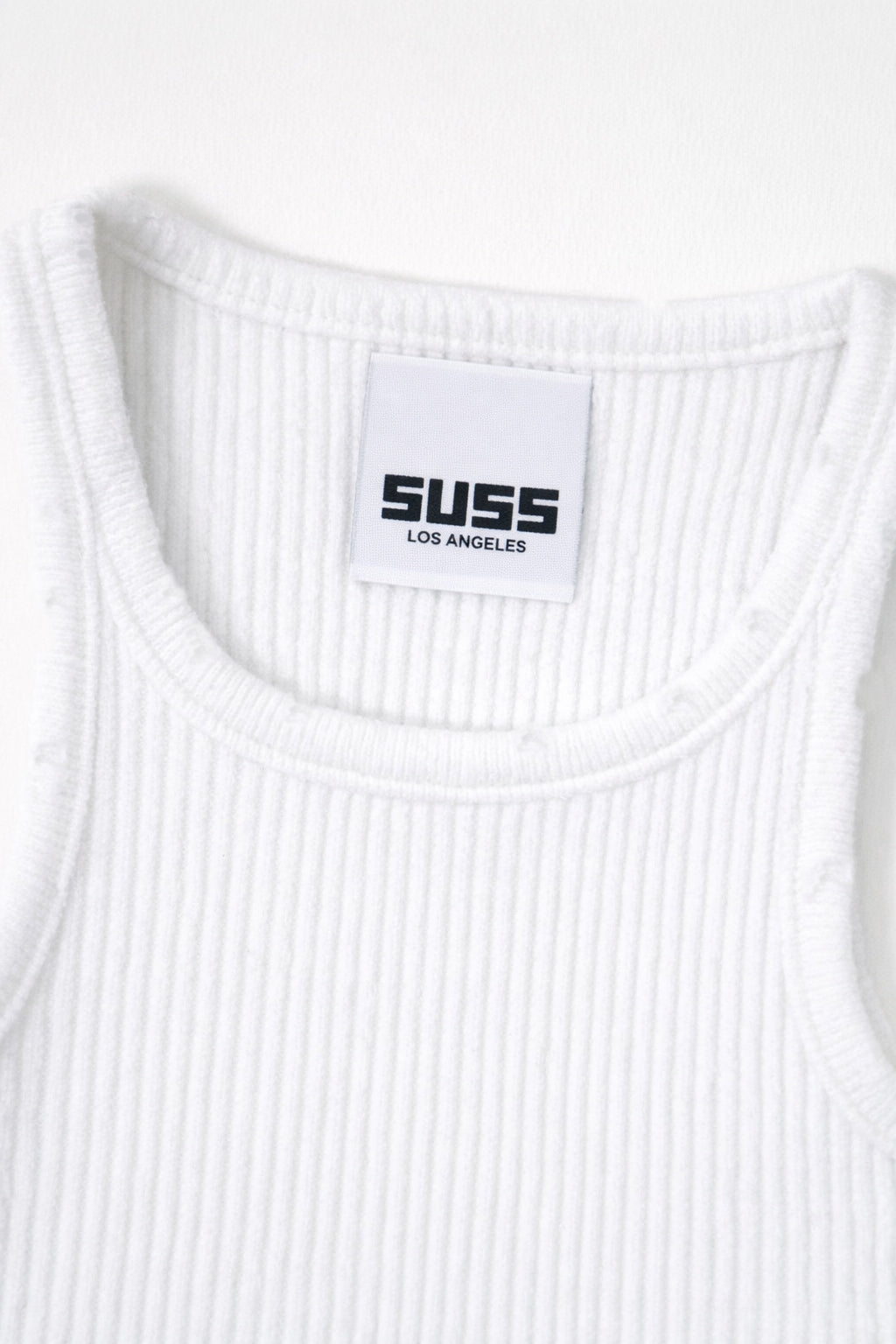 Close-up of white ribbed knit tank neckline with subtle tattered edge detail and Suss label