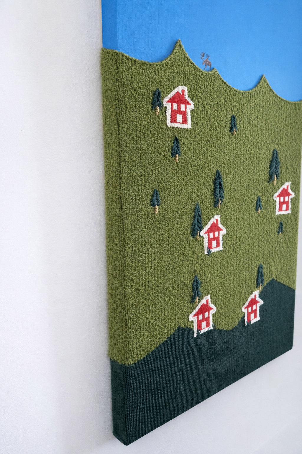 Detail of hand embroidered house on knitted wool landscape textile artwork and hand embroidered trees