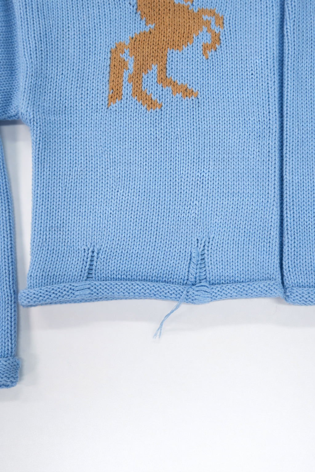 Hem detail of baby blue cotton cropped knit jacket with rolled edge finish