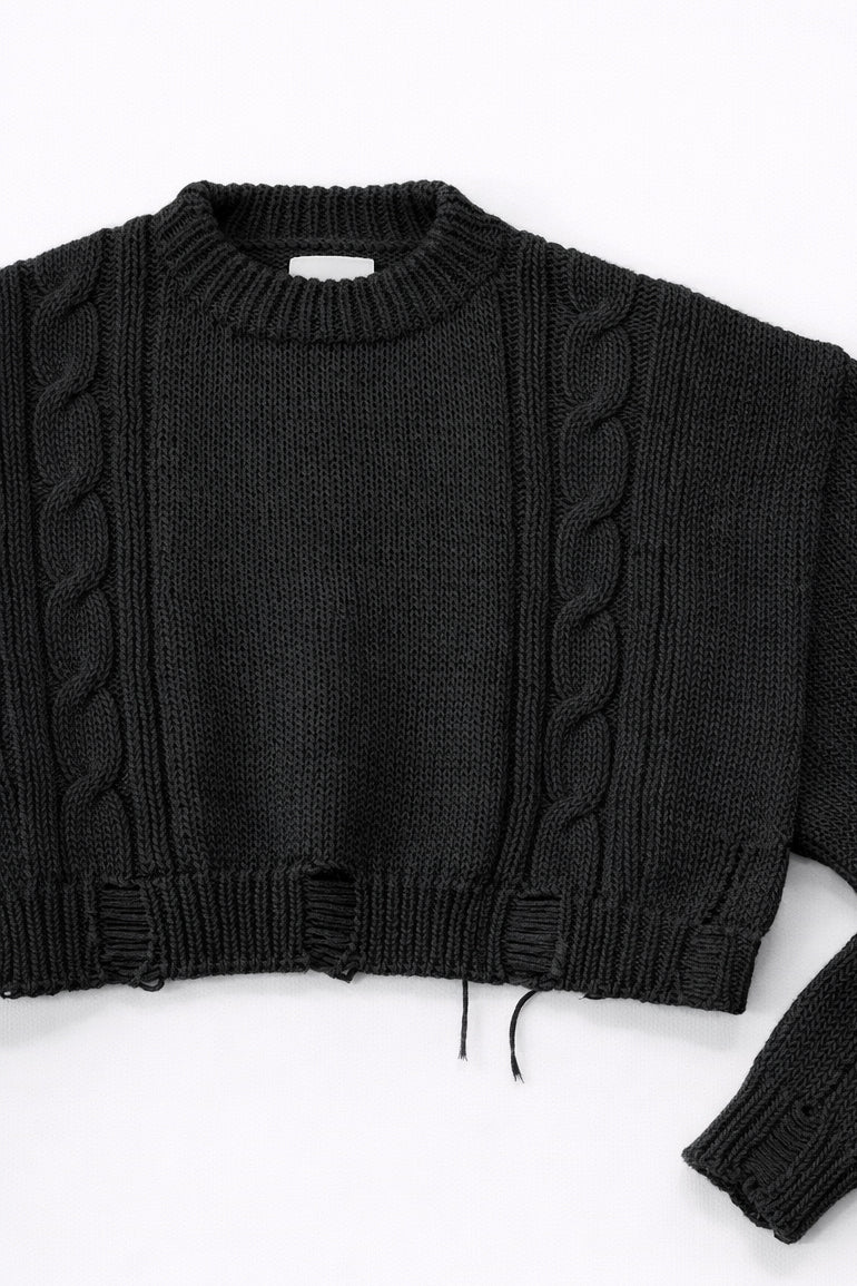Close up of sleeve on black cropped knit sweater showing texture and distressed stitch details