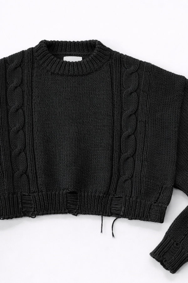 Close up of sleeve on black cropped knit sweater showing texture and distressed stitch details