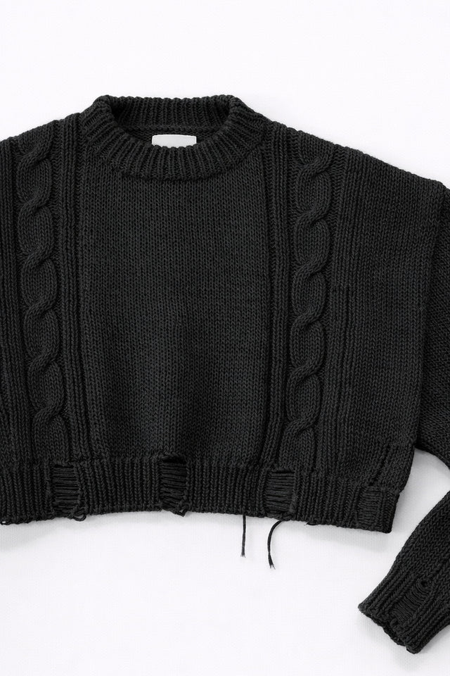 Close up of sleeve on black cropped knit sweater showing texture and distressed stitch details
