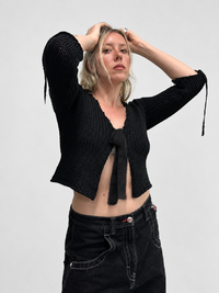 Black chunky cotton knit cardigan worn on female model with ribbon tie closure and three-quarter sleeves