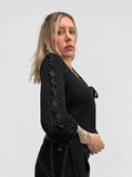 Black chunky cotton knit cardigan worn  on woman from the side showing ribbon detail along sleeve