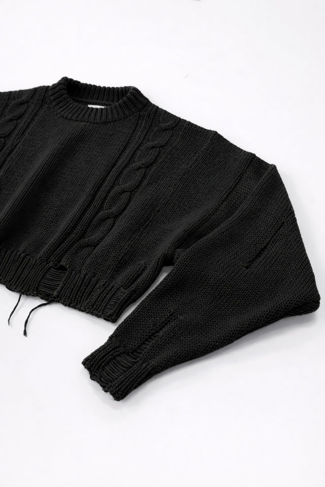 Close up of sleeve on black cropped knit sweater showing angle texture and distressed stitch detail