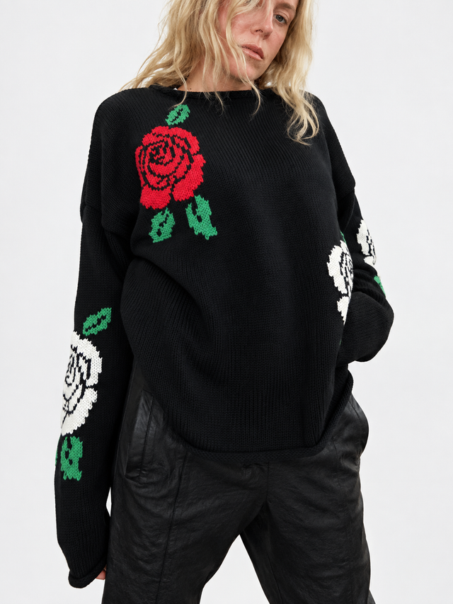 Suss knits black roll neck rose sweater with red and cream intarsia roses and green leaves shown on a woman with a light heather grey background