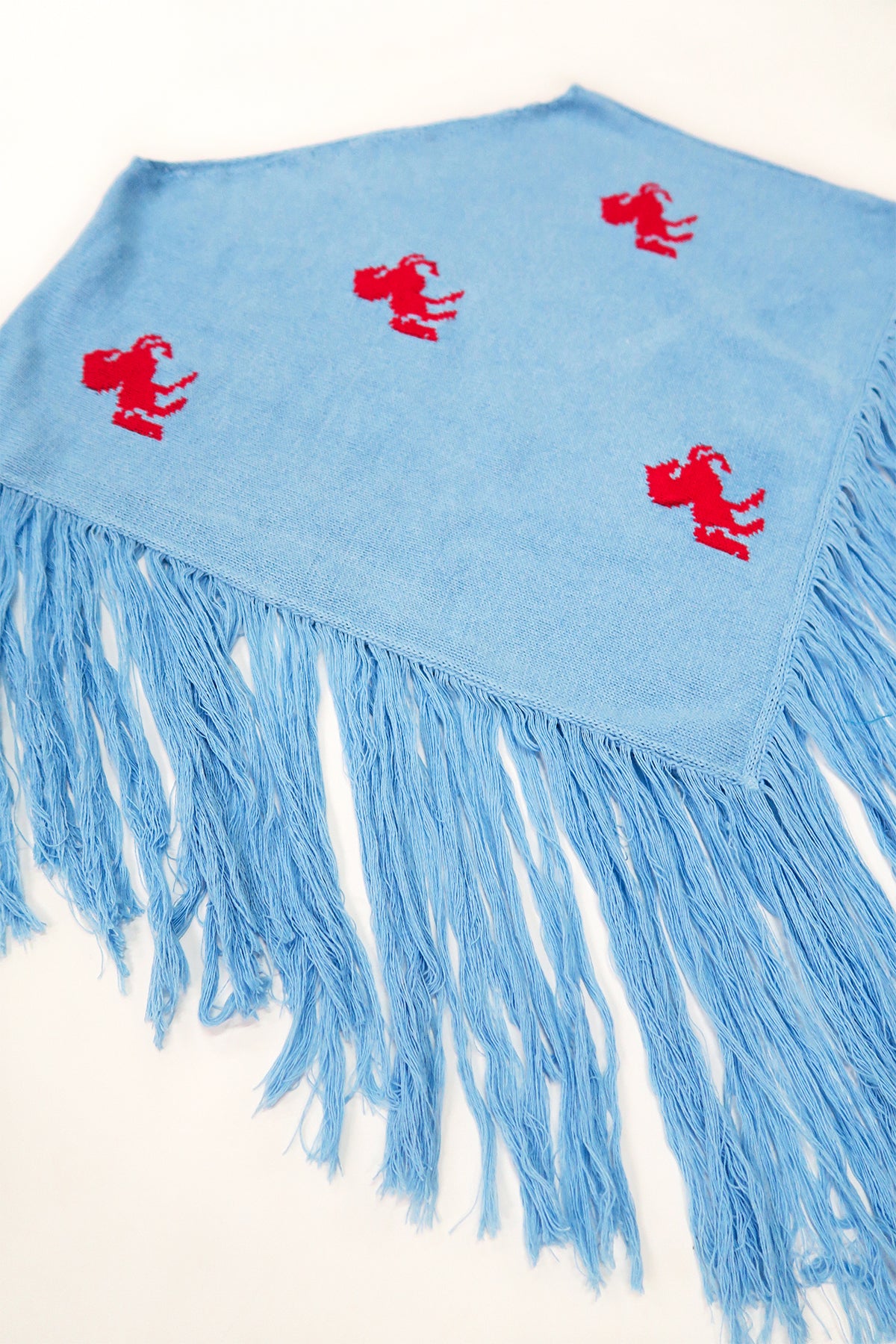 Angled view of blue cotton poncho with red horse motif and long fringe