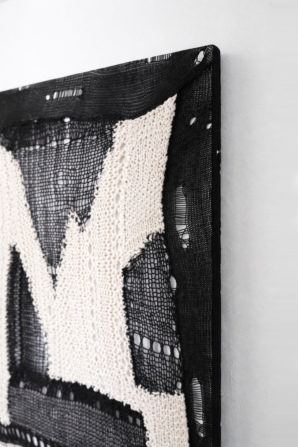 Close-up of black mesh and cream hand knit textile with varied yarn weights and open stitch detailing in abstract wall art