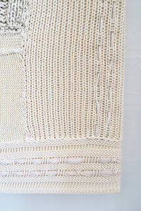 Close-up of right corner hand knit patchwork textile wall art showing mixed stitch patterns and textures in neutral cream tones