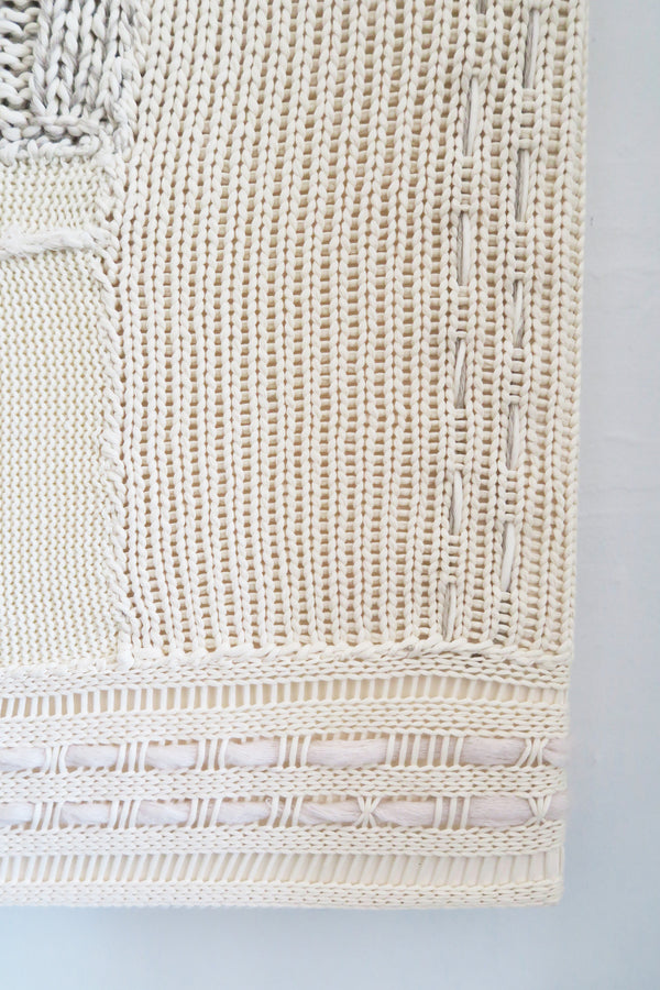 Close-up of right corner hand knit patchwork textile wall art showing mixed stitch patterns and textures in neutral cream tones