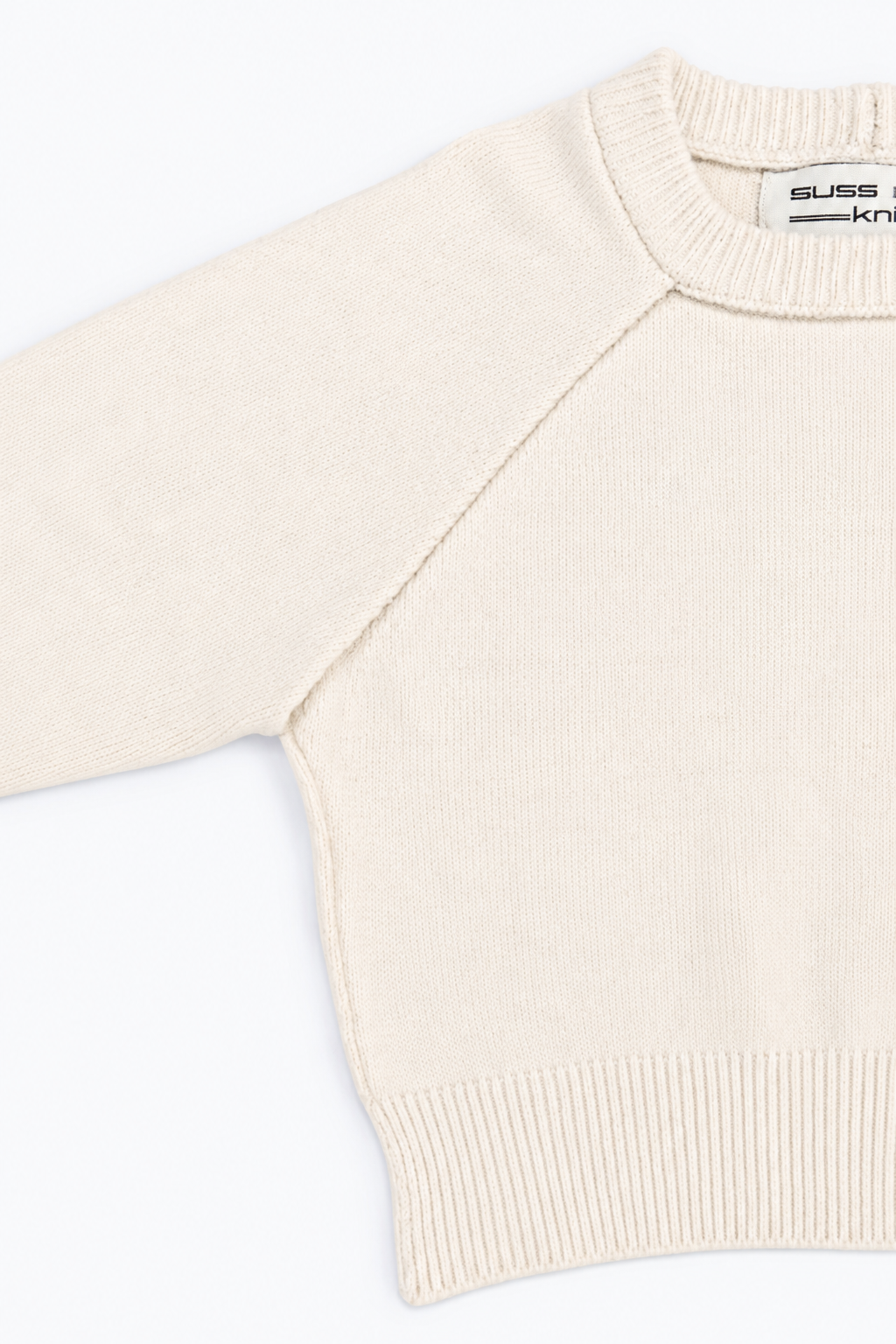 A close up of the Suss Cream Open Raglan Knit Top detail showing raglan construction and ribbed crewneck knit in cotton