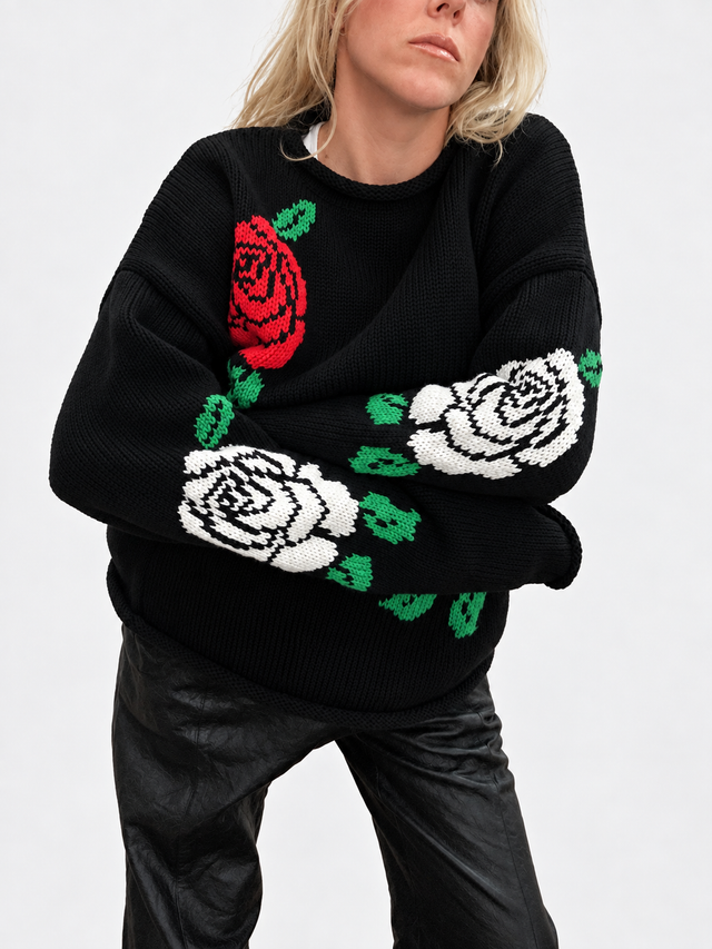 Suss knits detail photo of a woman wearing the black cotton rollneck sweater with arms crossed showing detail of the cream rose motif