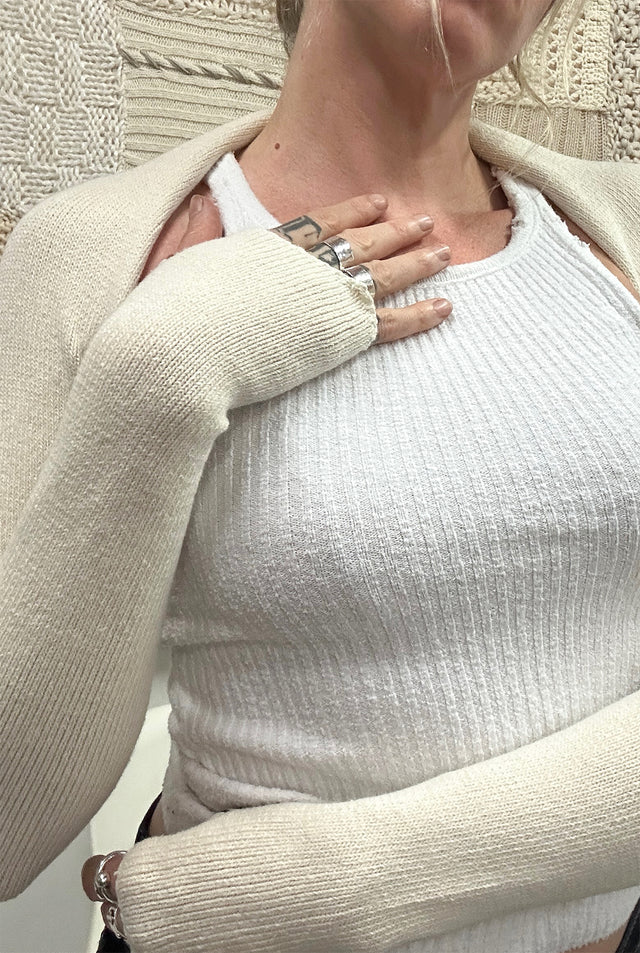 A close up of a female model wearing the Suss Hand Stitched Shrug in cream cotton showing a detail of the asymmetrical cuff on the shrug.