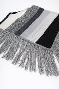 Angled view of black and grey, cotton, striped knit poncho with fringe detail