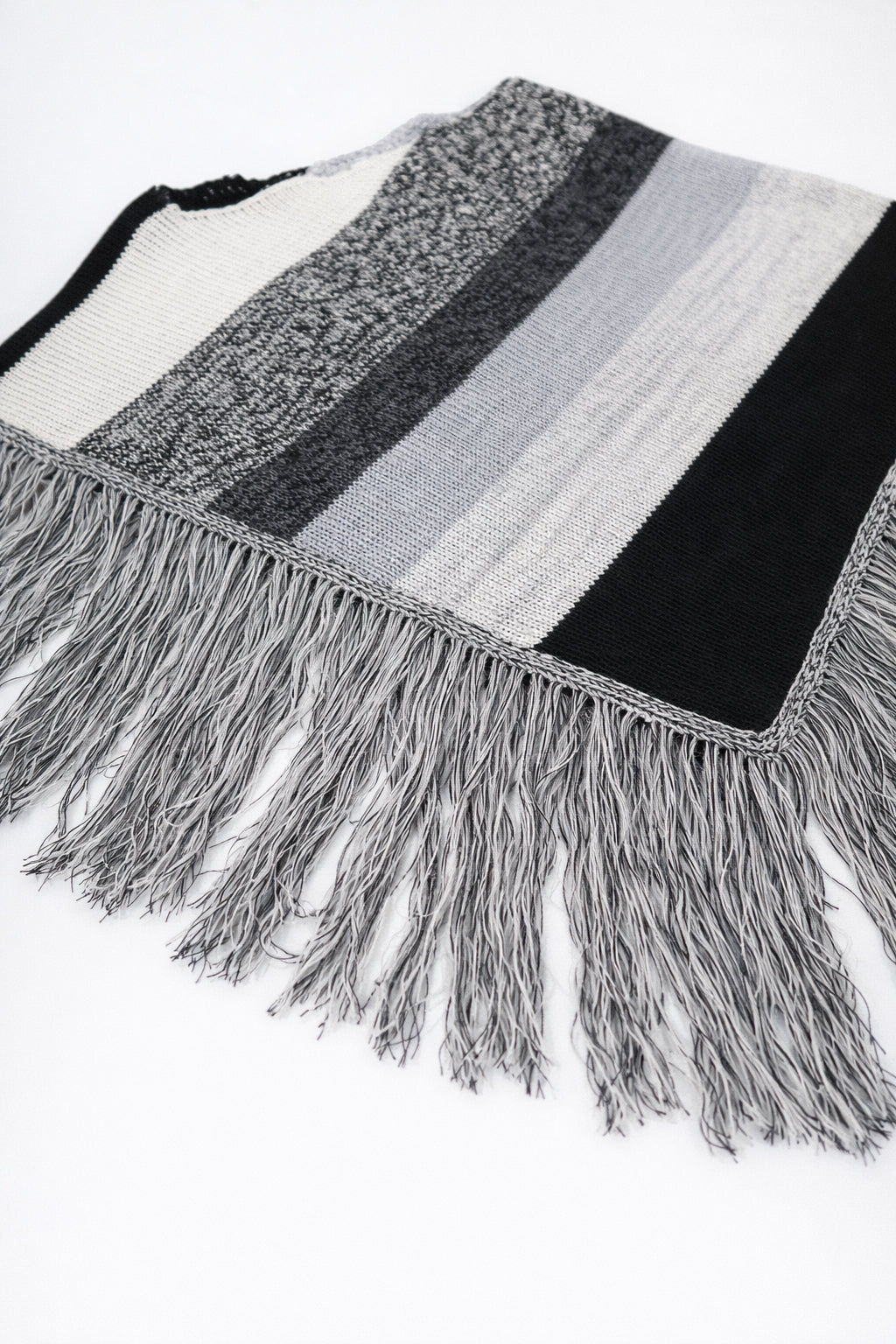 Angled view of black and grey, cotton, striped knit poncho with fringe detail