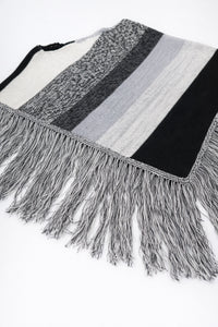 Angled view of black and grey, cotton, striped knit poncho with fringe detail