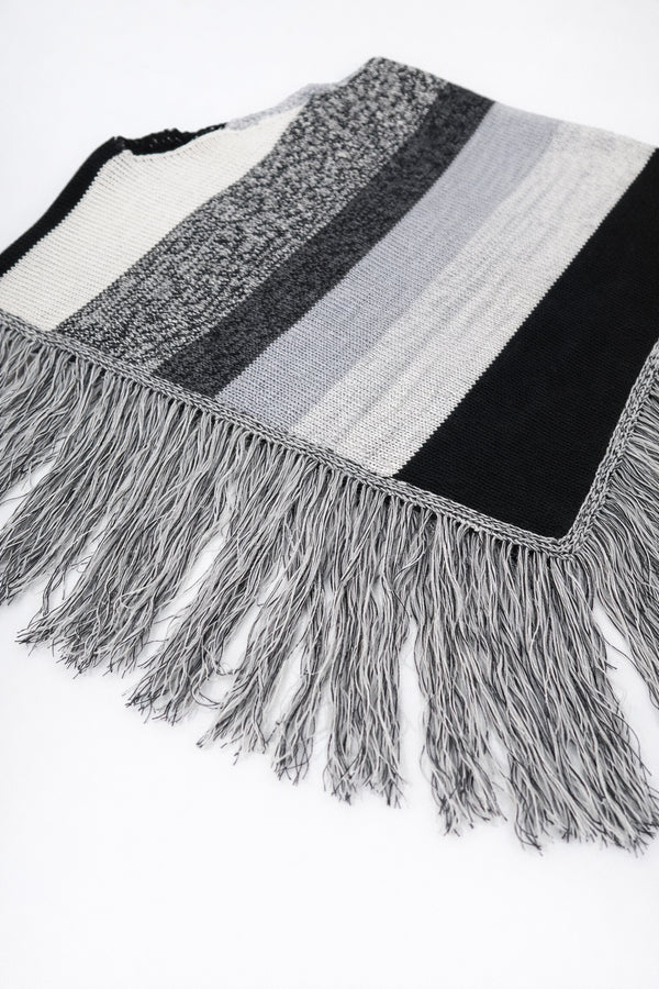 Angled view of black and grey, cotton, striped knit poncho with fringe detail