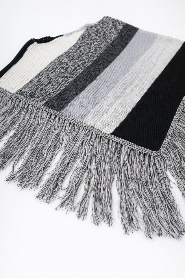 Angled view of black and grey, cotton, striped knit poncho with fringe detail