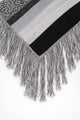 Close-up of long fringe detail on black and grey striped knit poncho