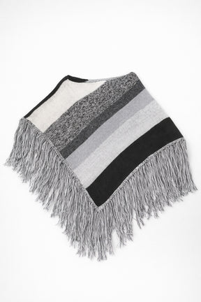 Black and grey striped knit cotton poncho with fringe laid flat on light grey background