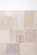 Close-up of hand knit patchwork textile wall art showing mixed stitch patterns and textures in neutral cream tones