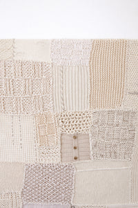 Close-up of hand knit patchwork textile wall art showing mixed stitch patterns and textures in neutral cream tones