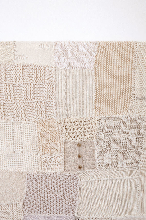 Close-up of hand knit patchwork textile wall art showing mixed stitch patterns and textures in neutral cream tones