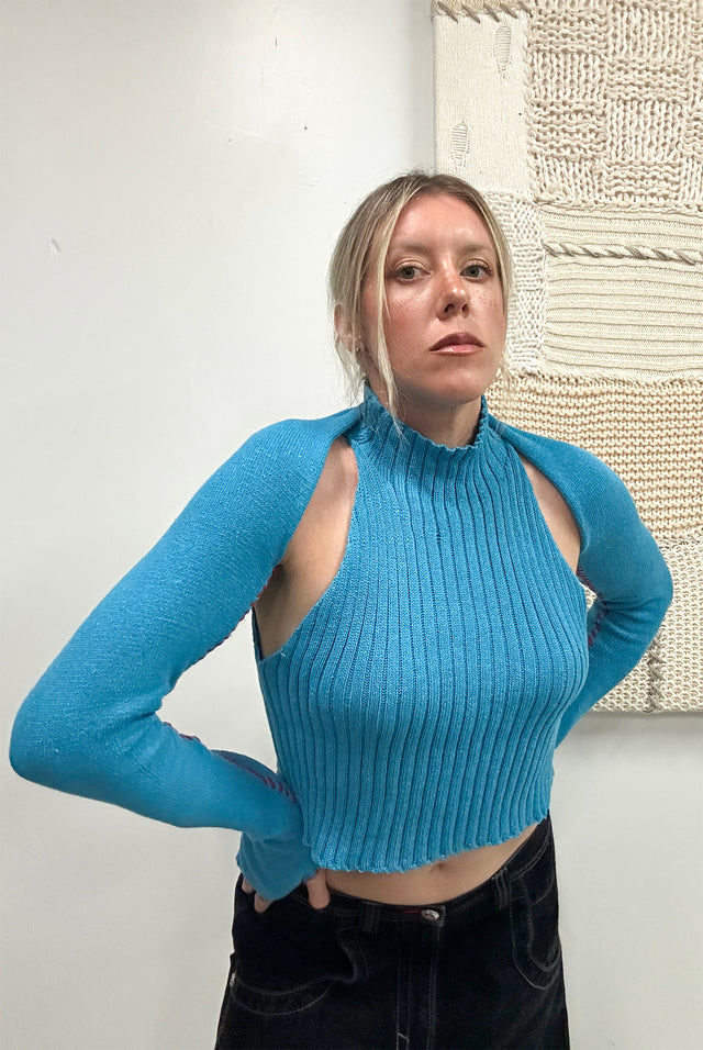 Suss Knits hand stitched shrug knit in turquoise cotton and lycra with a red accent whip stitch shown on body with thumbholes.