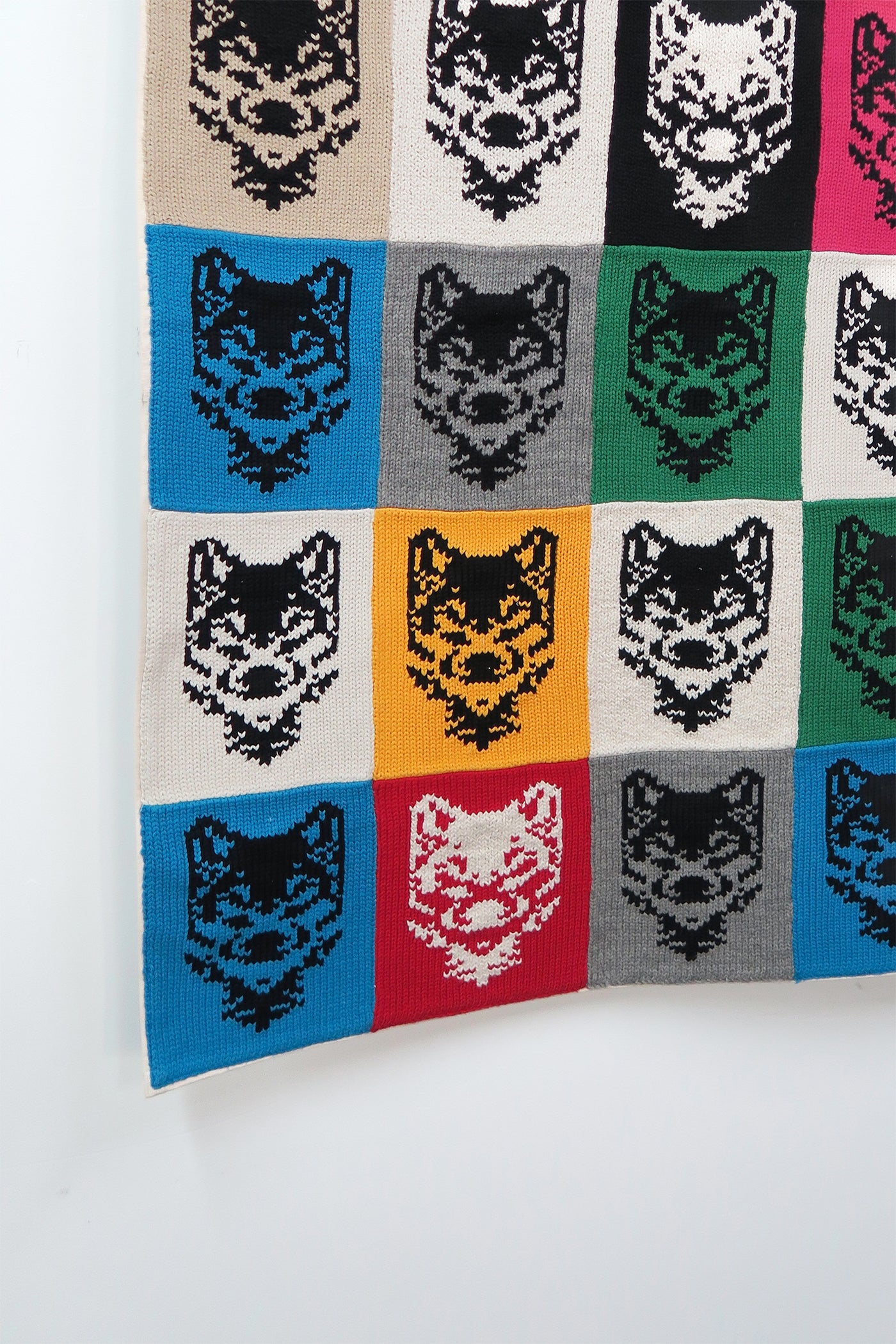 Angled detail of colorful wolf knit panels in grid layout on cotton fiber wall hanging
